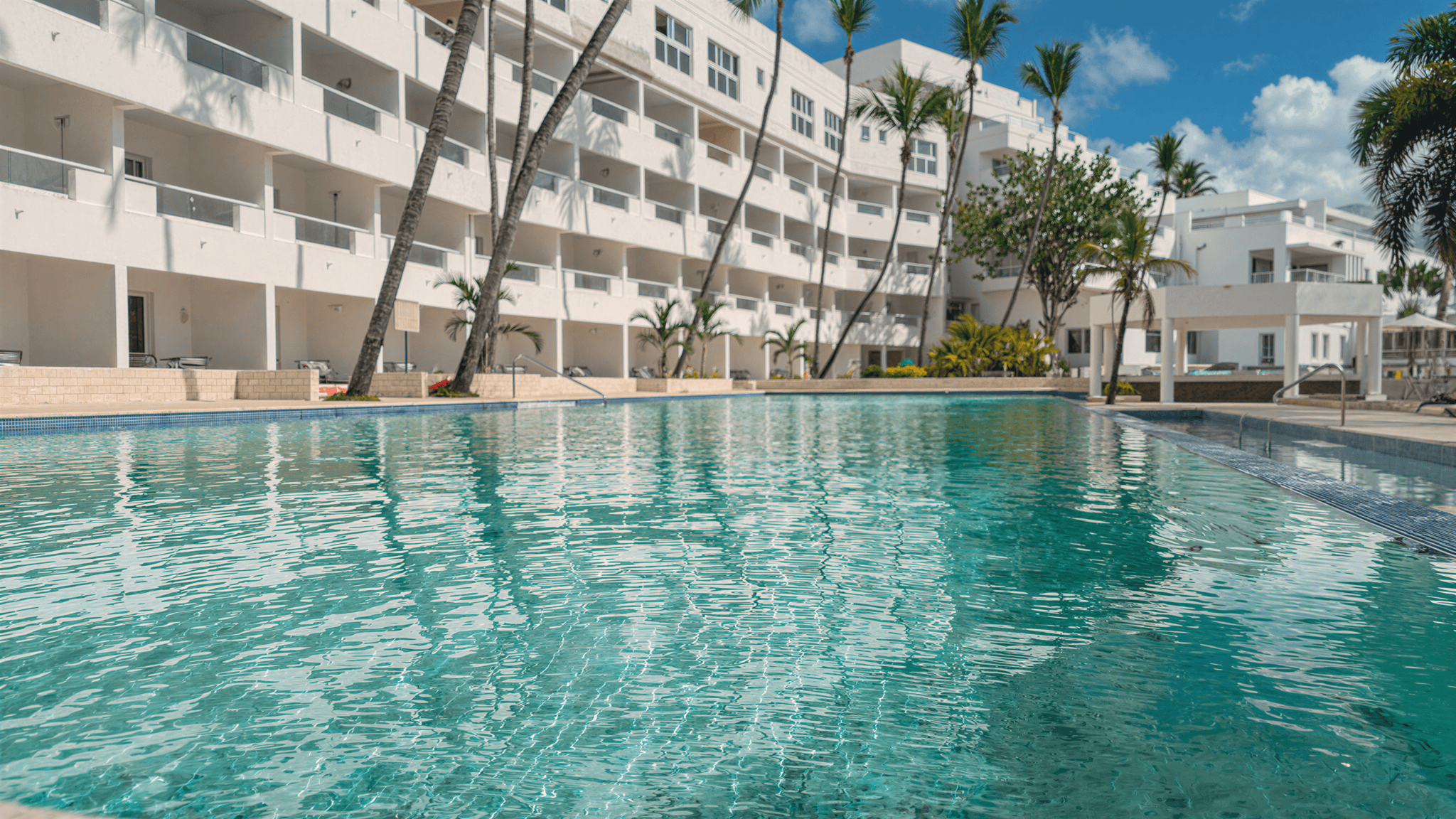 Relaxing pool at Santo Domingo Bay Boca Chica with modern white hotel buildings and palm trees.
